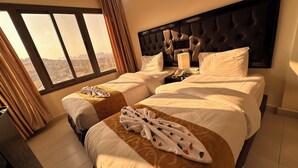 A hotel room with a large bed, a smaller bed, and a nightstand with a lamp. There is a window with curtains, and the room has a view of the city. - Sharah Mountains Hotel (Wadi Musa)