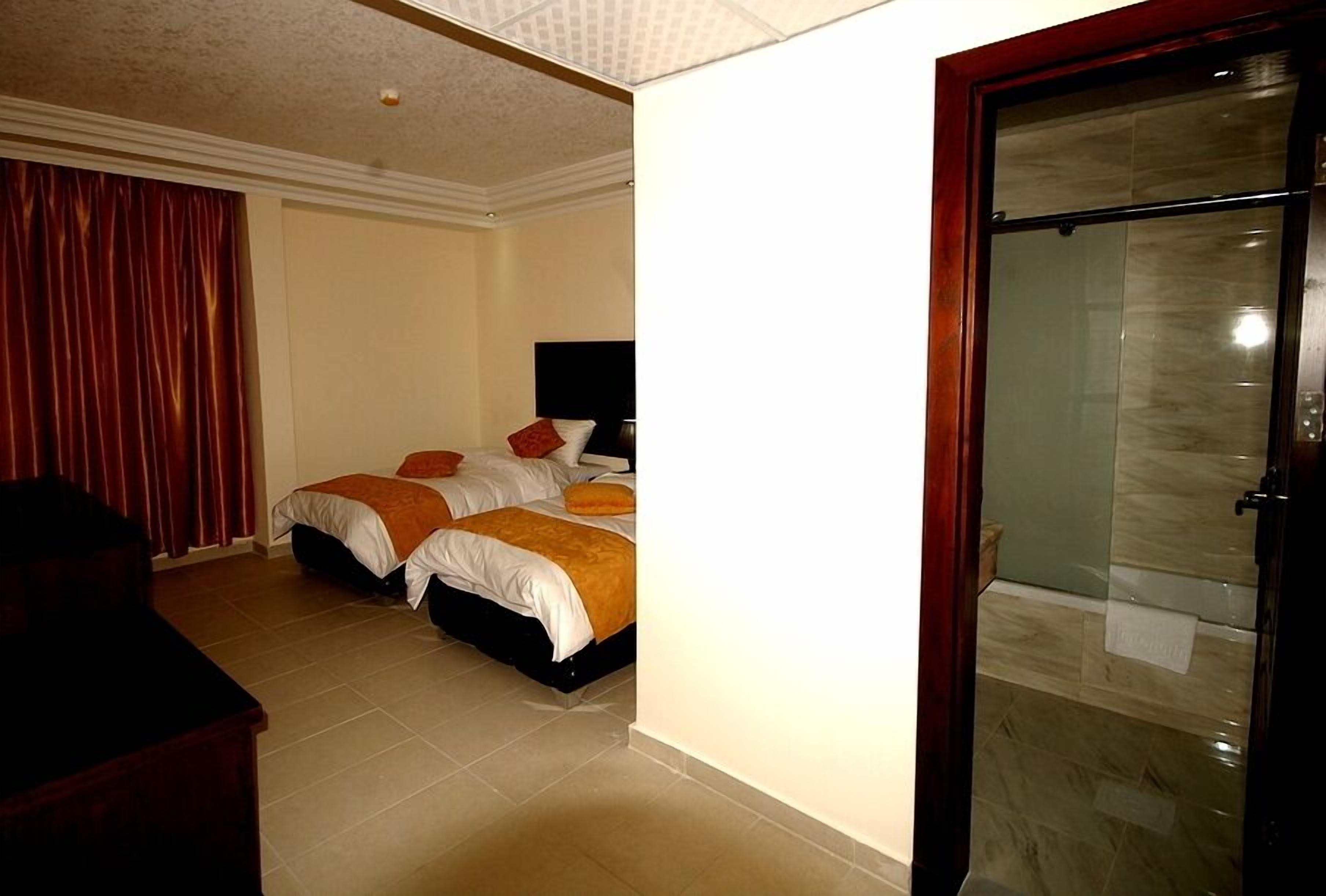 A hotel room with two beds, a desk, and a glass shower enclosure.