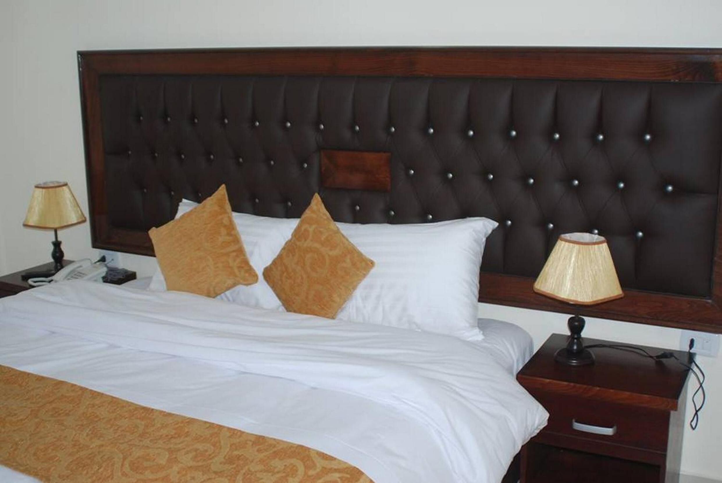 A neatly made bed with a dark headboard, two pillows, and a bedside table with a lamp.