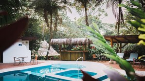 A pool area with a thatched structure, seating, and lush greenery. - Huasquila Amazon Lodge (Cotundo)