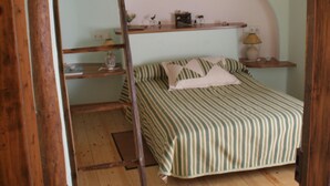 Een slaapkamer met een houten ladder, een bed met gestreepte beddengoed, een hoofdbord en een plank met diverse spullen.