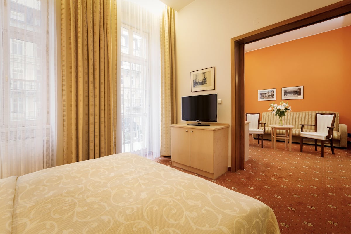 Ein Hotelzimmer mit Bett, Fernseher auf einer Holzkommode, einem kleinen Tisch mit Stühlen sowie zwei gerahmten Bildern an der Wand.