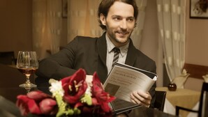 A man reading a book at a table with a glass of wine and flowers. - Venus (Karlovy Vary)