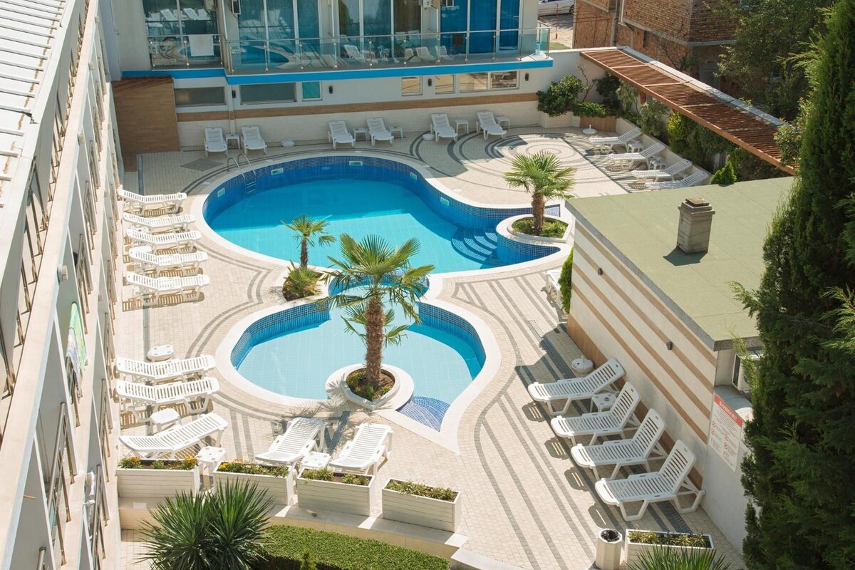 A rooftop swimming pool with multiple sun loungers and palm trees.