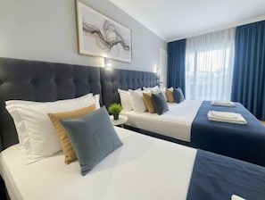 A hotel room with two beds, a large headboard, a wall-mounted artwork, and a window with curtains. - Eskada (Tsarevo)