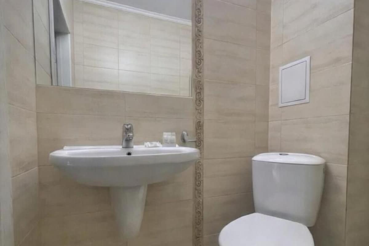 A bathroom with a sink, toilet, and a trash bin.