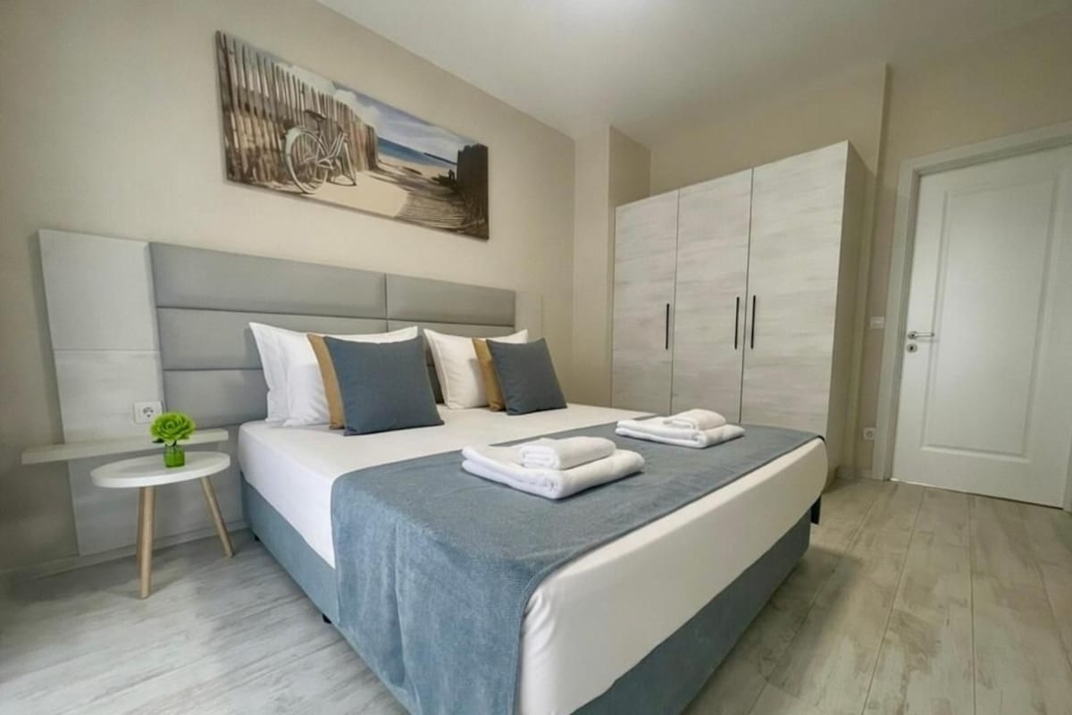 A modern bedroom with a large bed, a bedside table, a wardrobe, and a painting on the wall.
