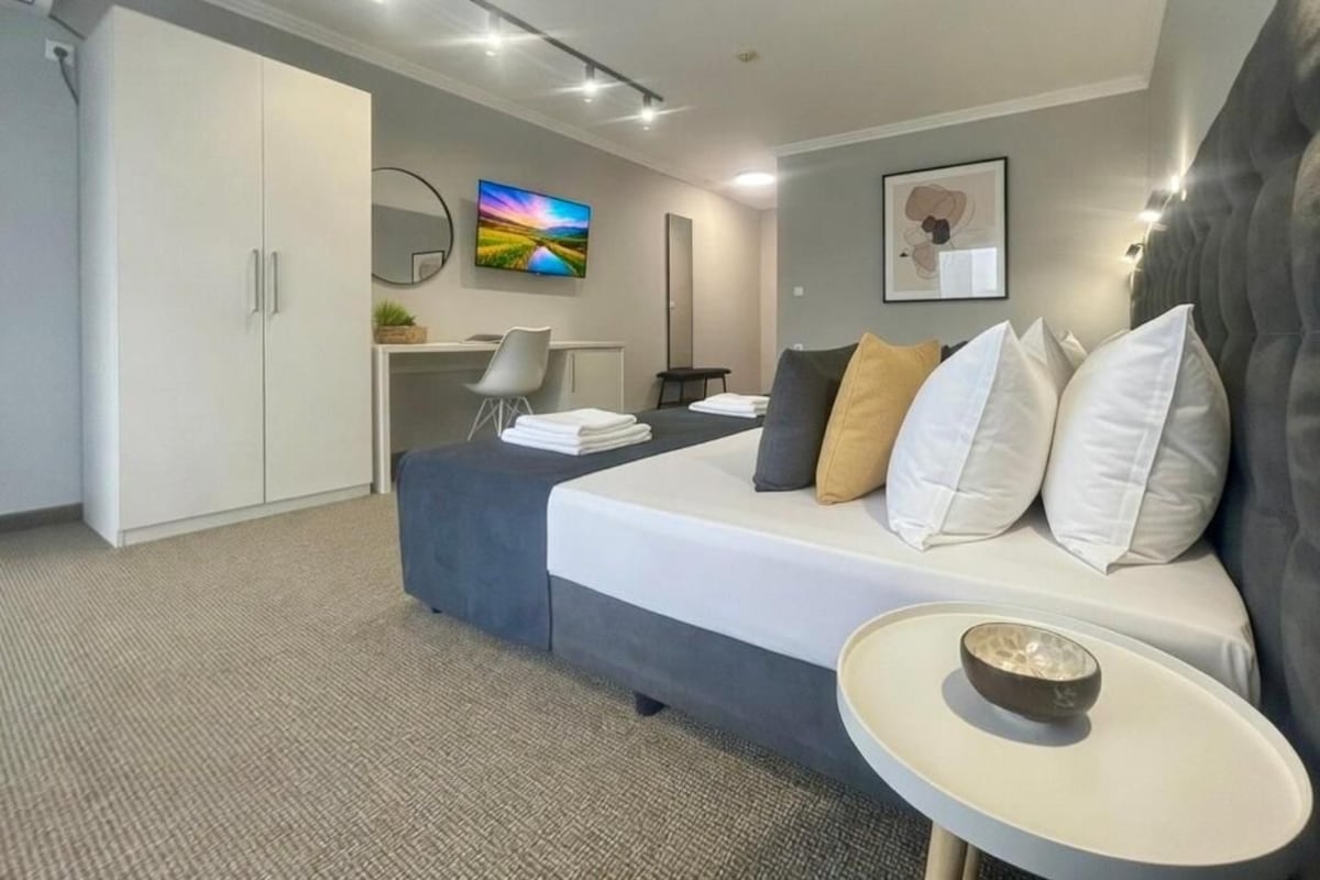 A modern hotel room with a bed, bedside table, and a desk area.