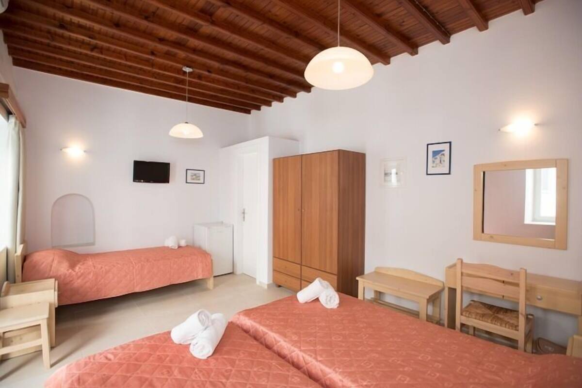 Habitación de hotel con dos camas, muebles de madera, un armario, un televisor y un espejo.