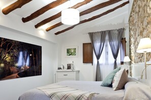 A bedroom with a bed, a nightstand, a lamp, a painting, and a window with curtains. - Cases Noves - Adults Only (El Castell de Guadalest)