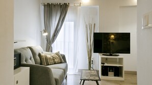 A modern living room with a sofa, a TV, and a small table with speakers.