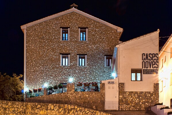 A stone building with multiple windows, a sign for 'CASAS NOVES' indicating it is a hotel, and outdoor seating with potted plants. - Cases Noves - Adults Only (El Castell de Guadalest)