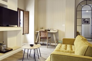 A living room with a television, a small table, a yellow sofa, and a wooden desk with a chair. - Cases Noves - Adults Only (El Castell de Guadalest)