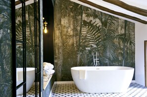 A modern bathroom with a freestanding bathtub, a large mirror, and a wall mural of tropical foliage. - Cases Noves - Adults Only (El Castell de Guadalest)