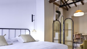 A neatly made bed with white linens and two pillows, a small desk with a chair, and a hanging light fixture.