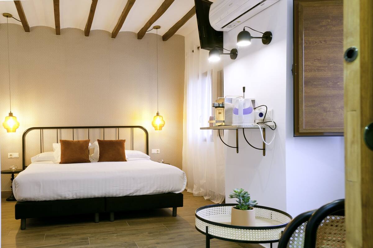 A bedroom with a bed, bedside lamps, a small table with a plant, and a wall-mounted shelf with toiletries.