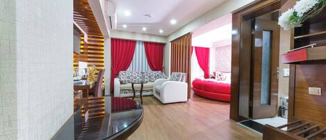 A modern living room with a sofa, a dining table, and a red accent wall.