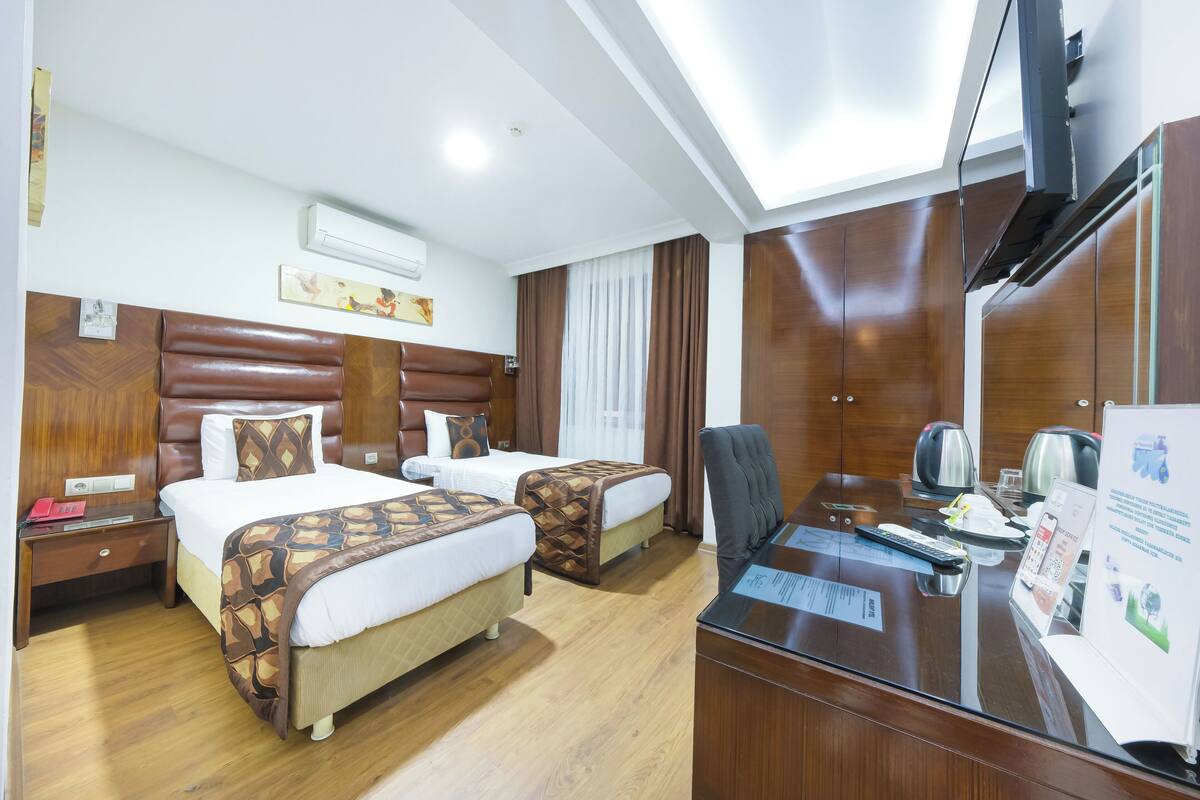 Een hotelkamer met twee bedden, een bureau met een computer, een spiegel en een televisie.