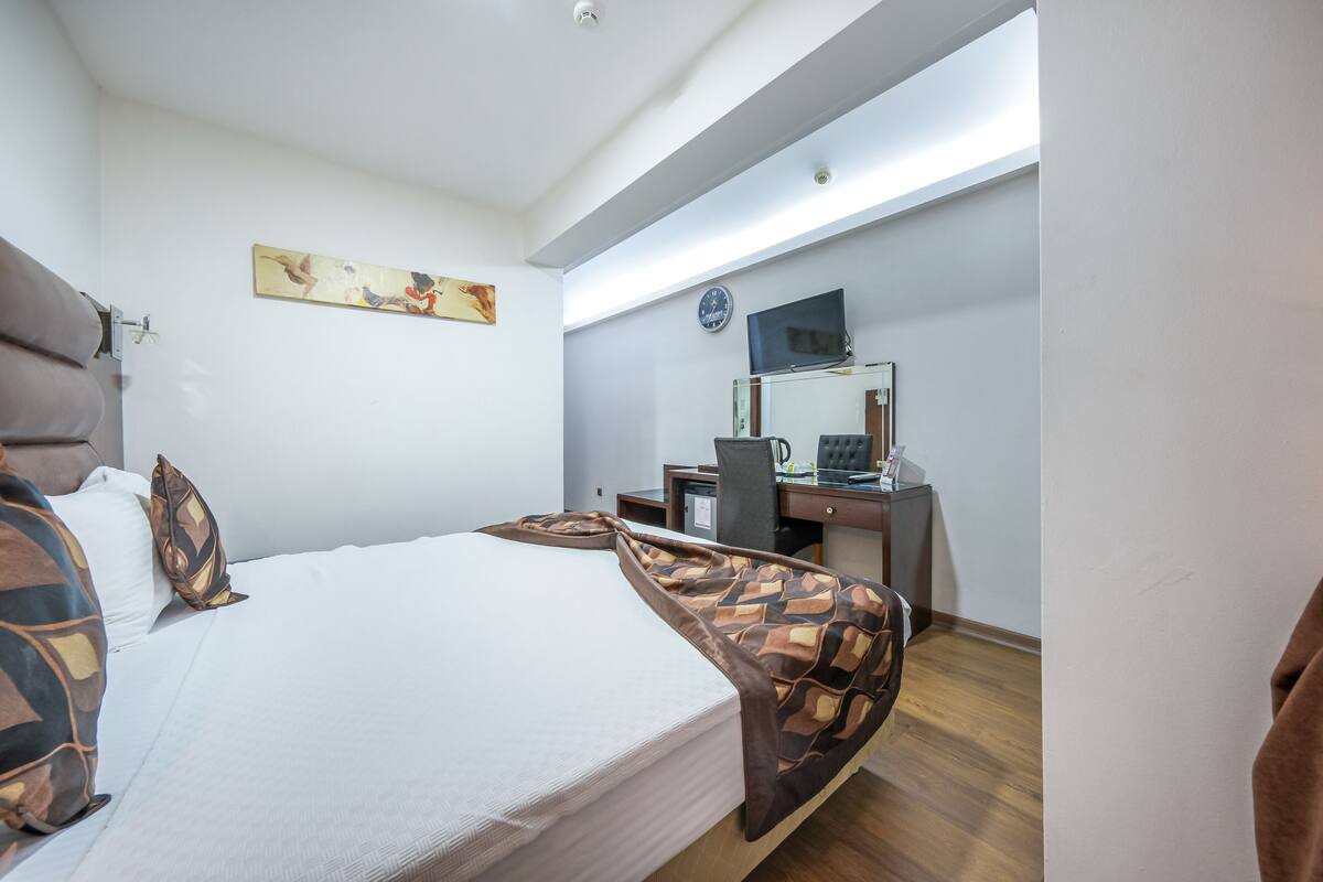 Een hotelkamer met een bed, een bureau, een stoel, een klok en een schilderij aan de muur.