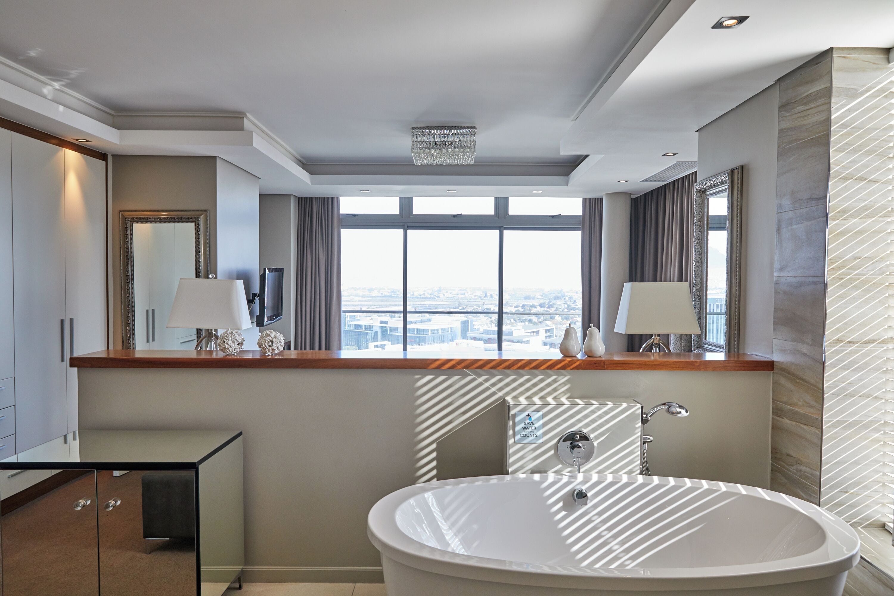 Een moderne badkamer met een ruime badkuip, een wastafel met spiegel, en een stadszicht door grote ramen.