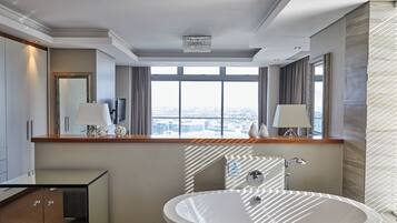 Een moderne badkamer met een ruime badkuip, een wastafel met spiegel, en een stadszicht door grote ramen.