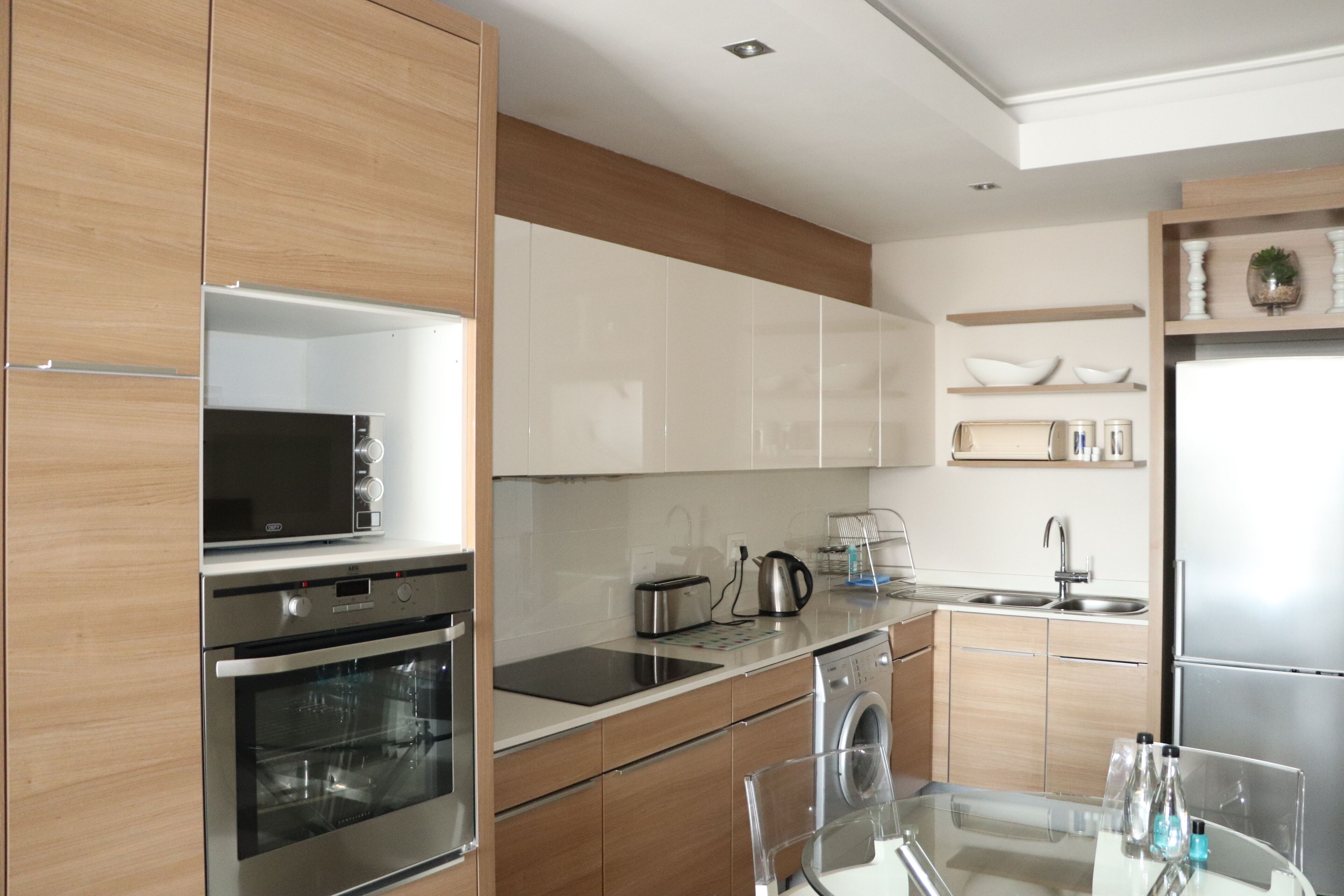 A modern kitchen with stainless steel appliances, wooden cabinets, and a glass dining table.