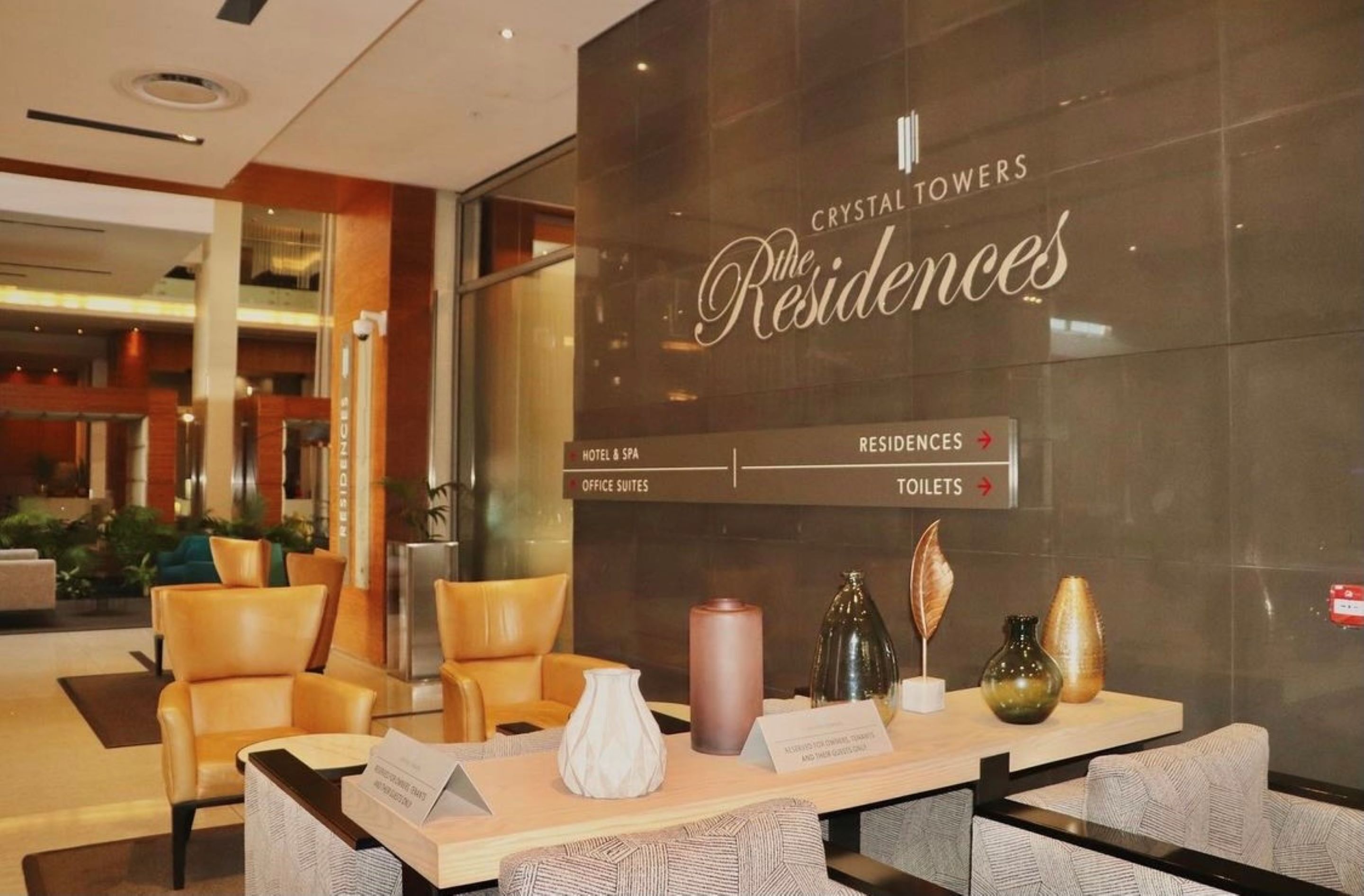A hotel lobby with a reception desk, seating area, and directional signs for hotel rooms, office suites, and toilets.
