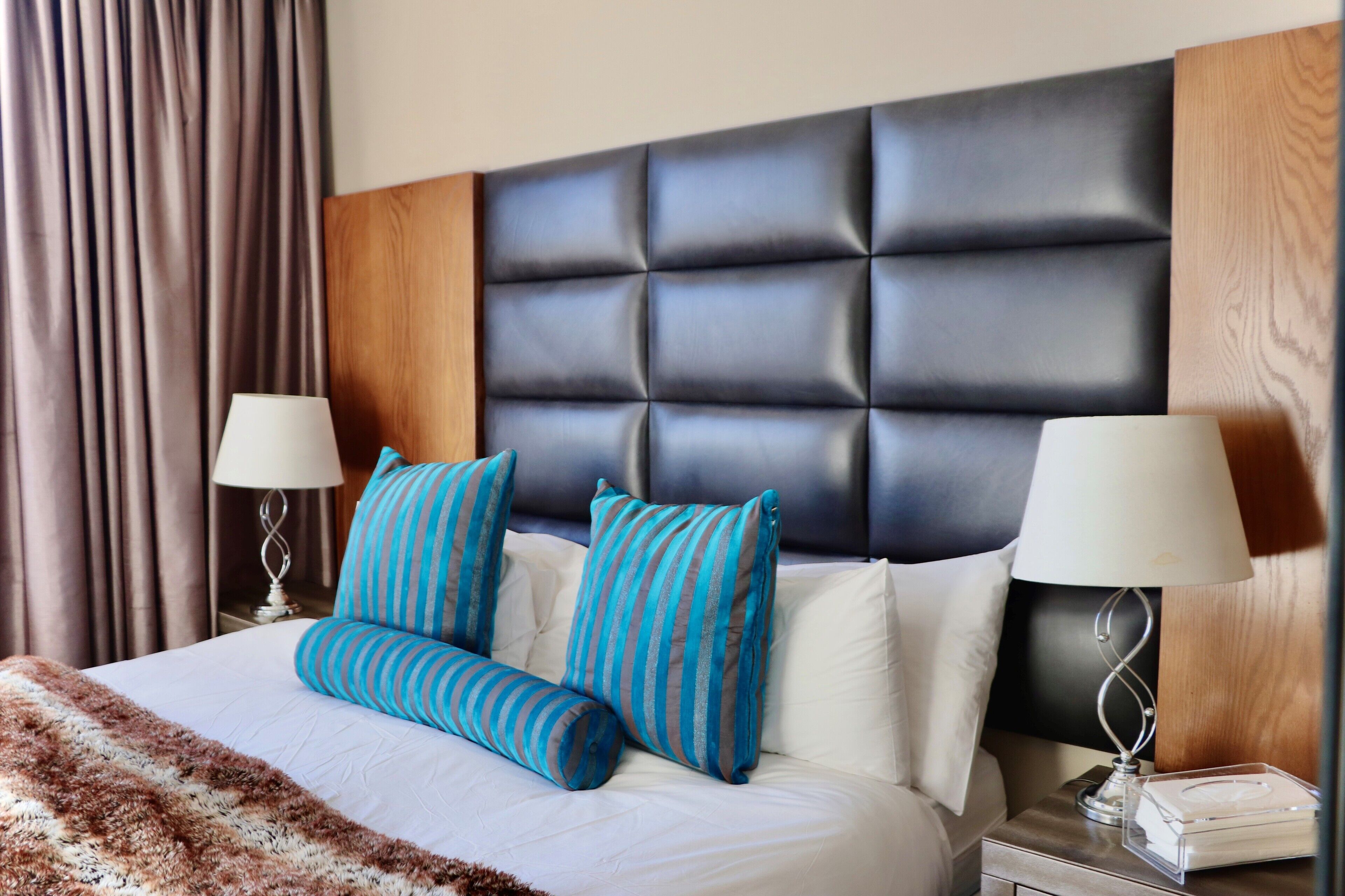 A neatly made bed with striped pillows, a fluffy blanket, and a headboard with a wooden panel.