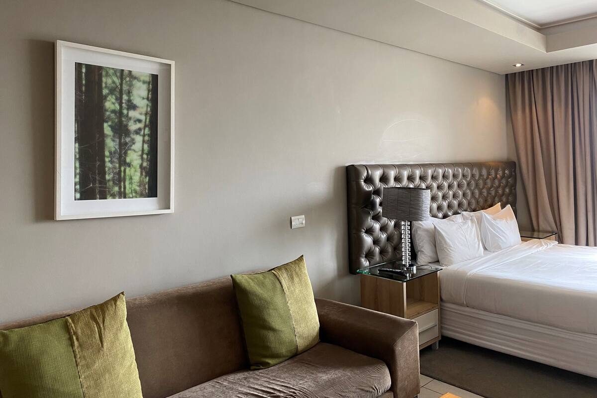 Ein Hotelzimmer mit einem großen Bett, einem braunen Sofa, einem gerahmten Bild an der Wand und einem Nachttisch mit Lampe.