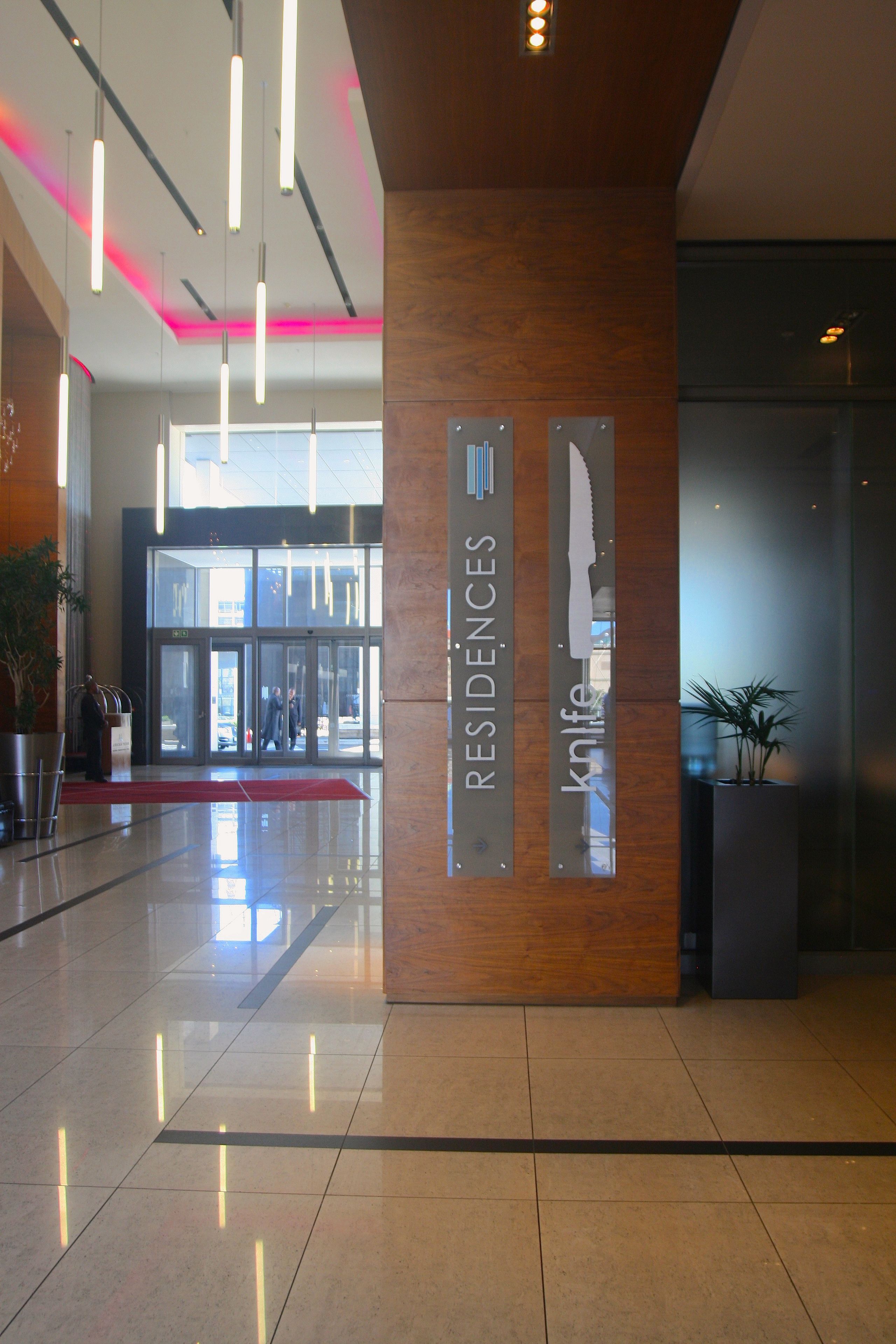 A modern hotel lobby with a polished floor, a red carpet, and a sign indicating 'RESIDENCES' and 'Knife' services.