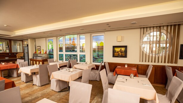 A restaurant with multiple tables and chairs, large windows with artwork, and a view of a building outside.