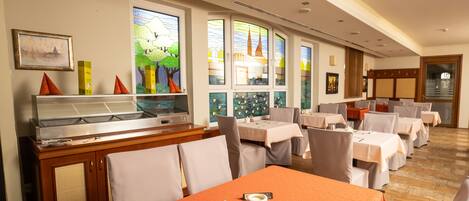 A restaurant with multiple tables, a buffet area, and large windows with artwork.
