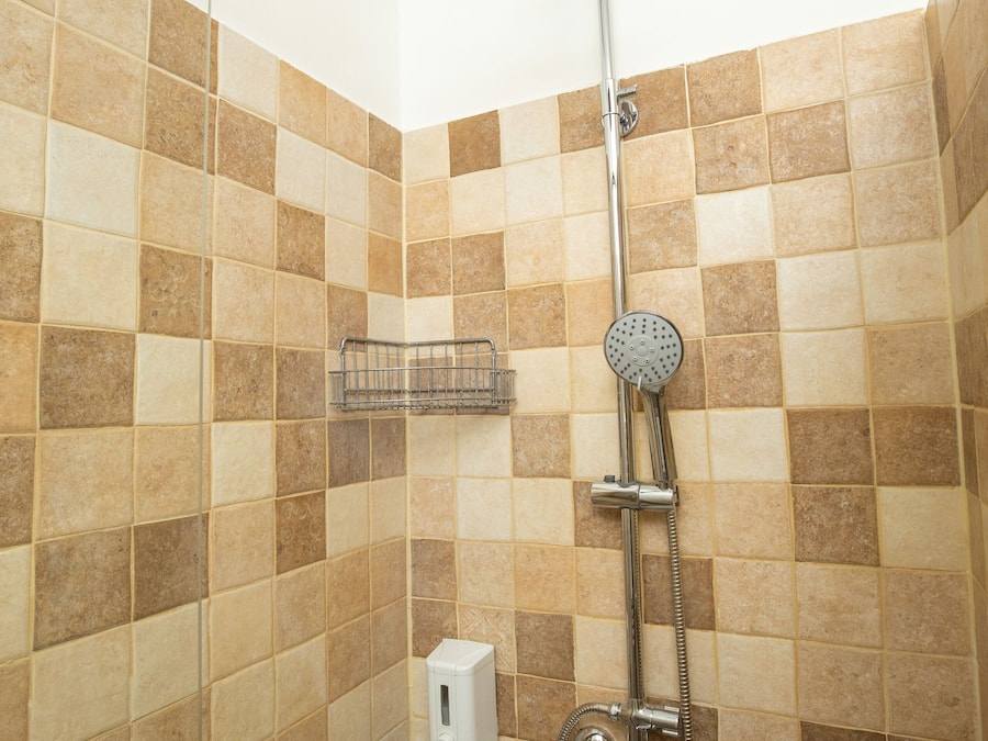 Une douche équipée d’un pommeau de douche à main et d’un robinet fixé au mur.