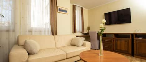 A living room with a beige sofa, a wooden coffee table, a flat-screen TV, and a wooden cabinet.