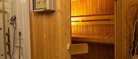 A sauna with wooden walls and a glass door, a control panel, and a towel rack.