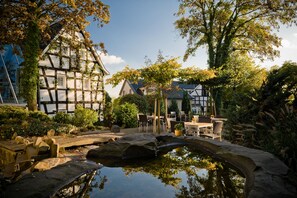A traditional half-timbered house with a garden patio, a pond, and outdoor seating. - Malerwinkel Hotel (Bergisch Gladbach)
