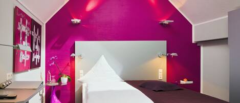A bedroom with a sloped ceiling, a bed, a desk, and a chair.
