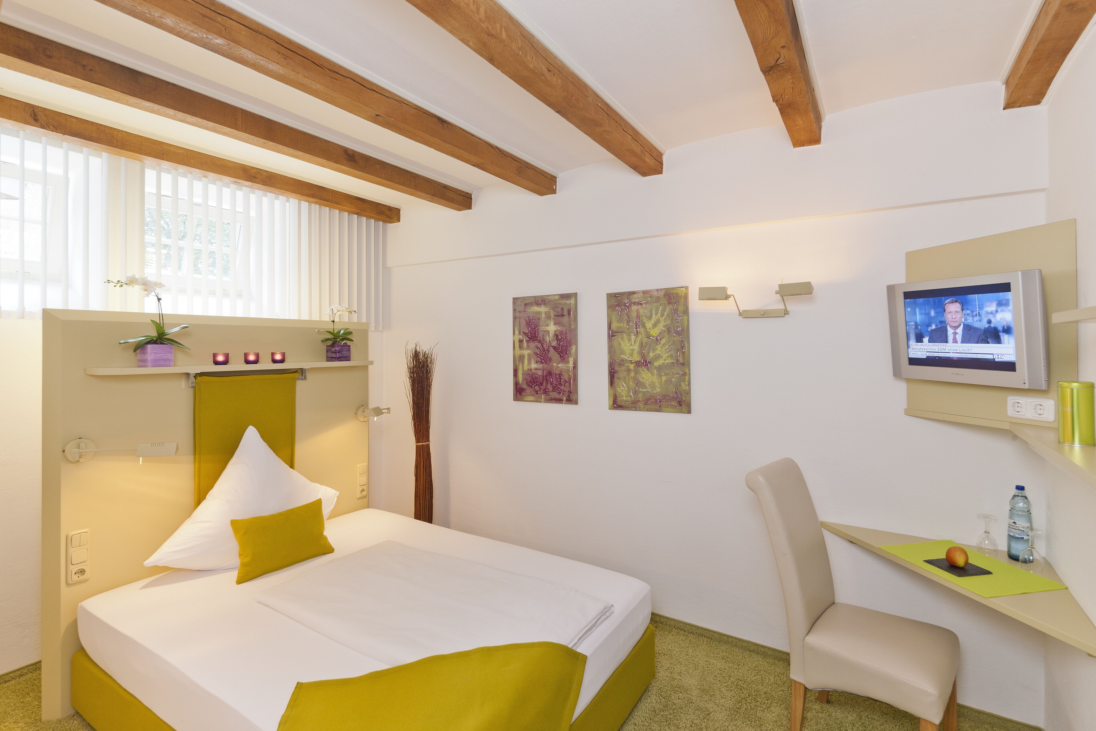 Een hotelkamer met een bed, een bureau, een stoel, een televisie en kunstwerken aan de muur.