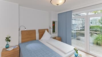 Ein modernes Schlafzimmer mit einem großen Bett, einem Holz-Kopfteil, Nachttischen, einem Beistelltisch, einem Fenster mit Blick auf Grünflächen und einer Deckenleuchte.