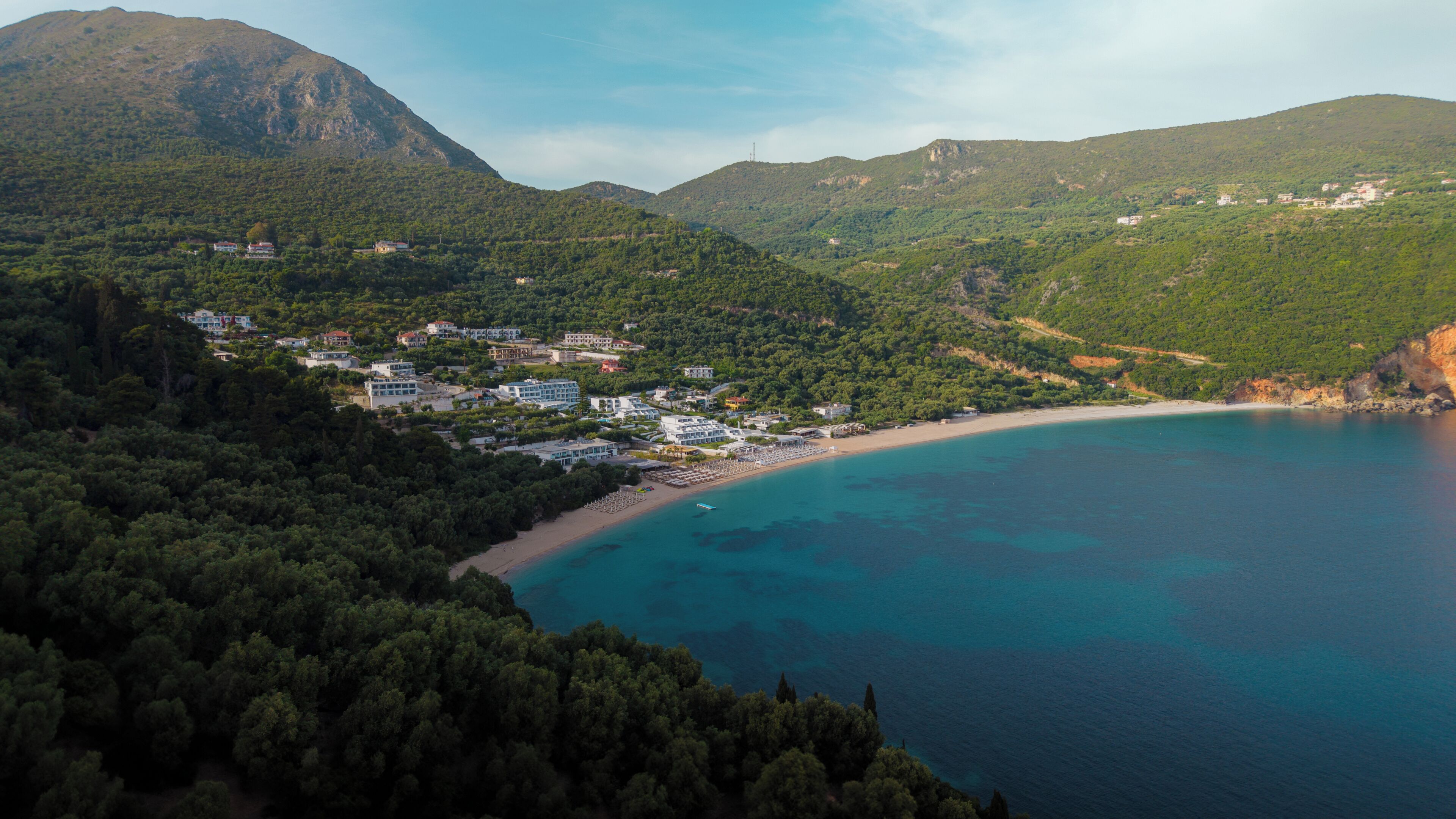 A coastal town with buildings surrounded by dense forest and mountains.