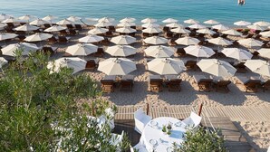 A beach with numerous sun loungers and umbrellas, a wooden deck area, and a view of the sea. - Lichnos Beach Hotel & Suites (Parga)