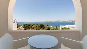 Un balcón con una mesa redonda y dos sillas, con vistas a la costa, edificios y árboles.