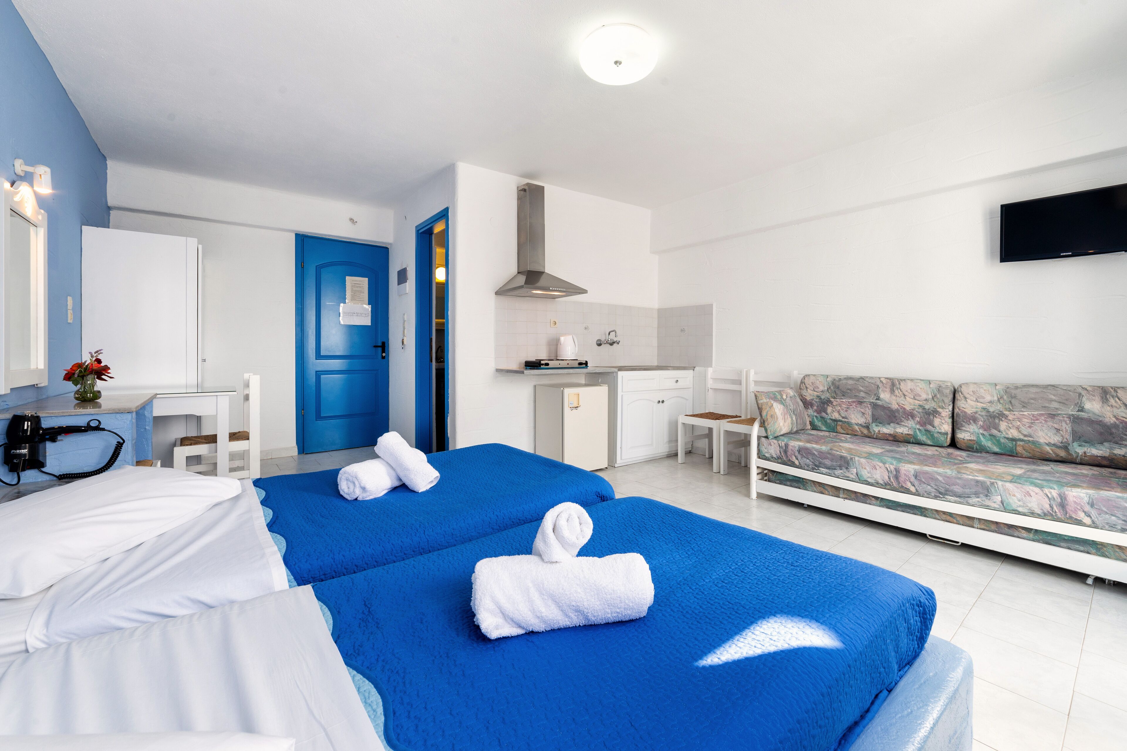 A hotel room with two beds, a kitchenette, a TV, and a sofa.