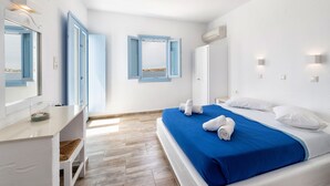 Una habitación de hotel con cama, escritorio, espejo y ventana con contraventanas azules.