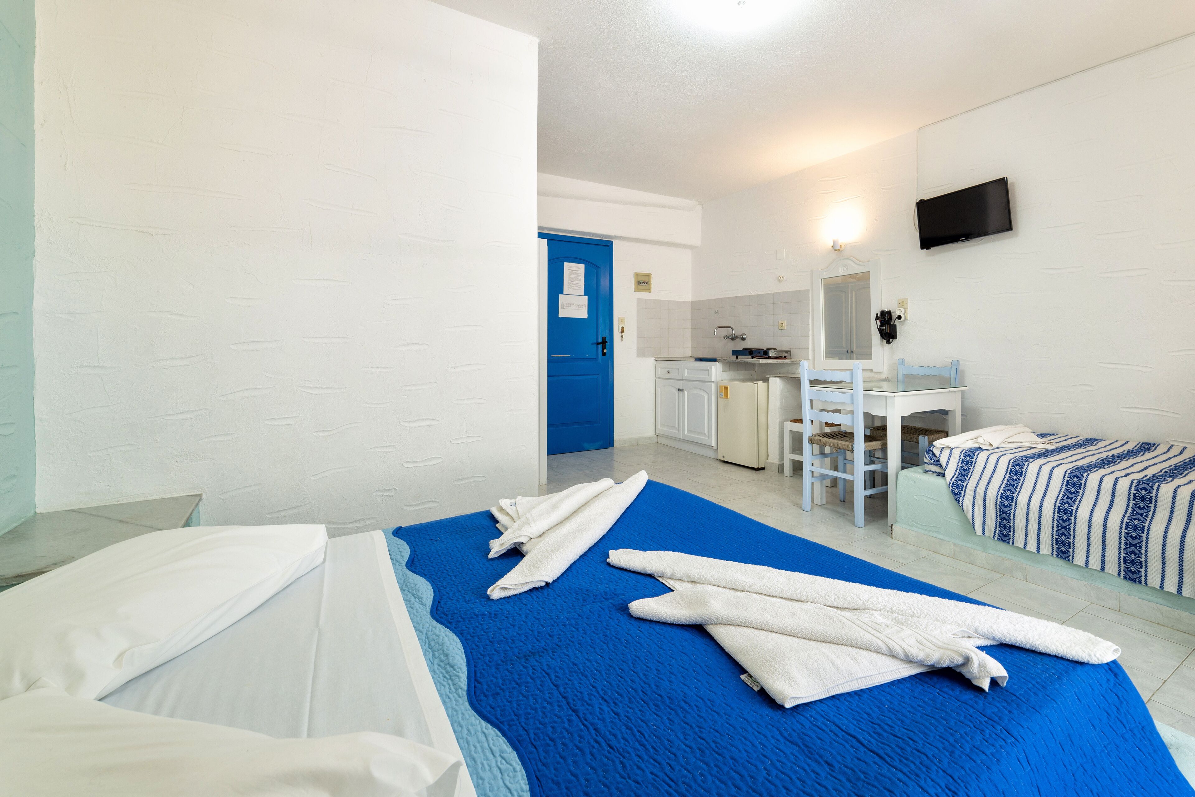 A hotel room with two beds, a bathroom, a kitchenette, and a TV mounted on the wall.