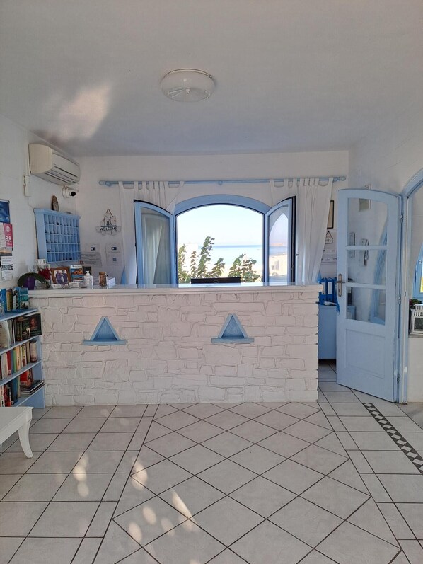 A reception area with a stone counter, a blue-framed window, and a view of the sea.