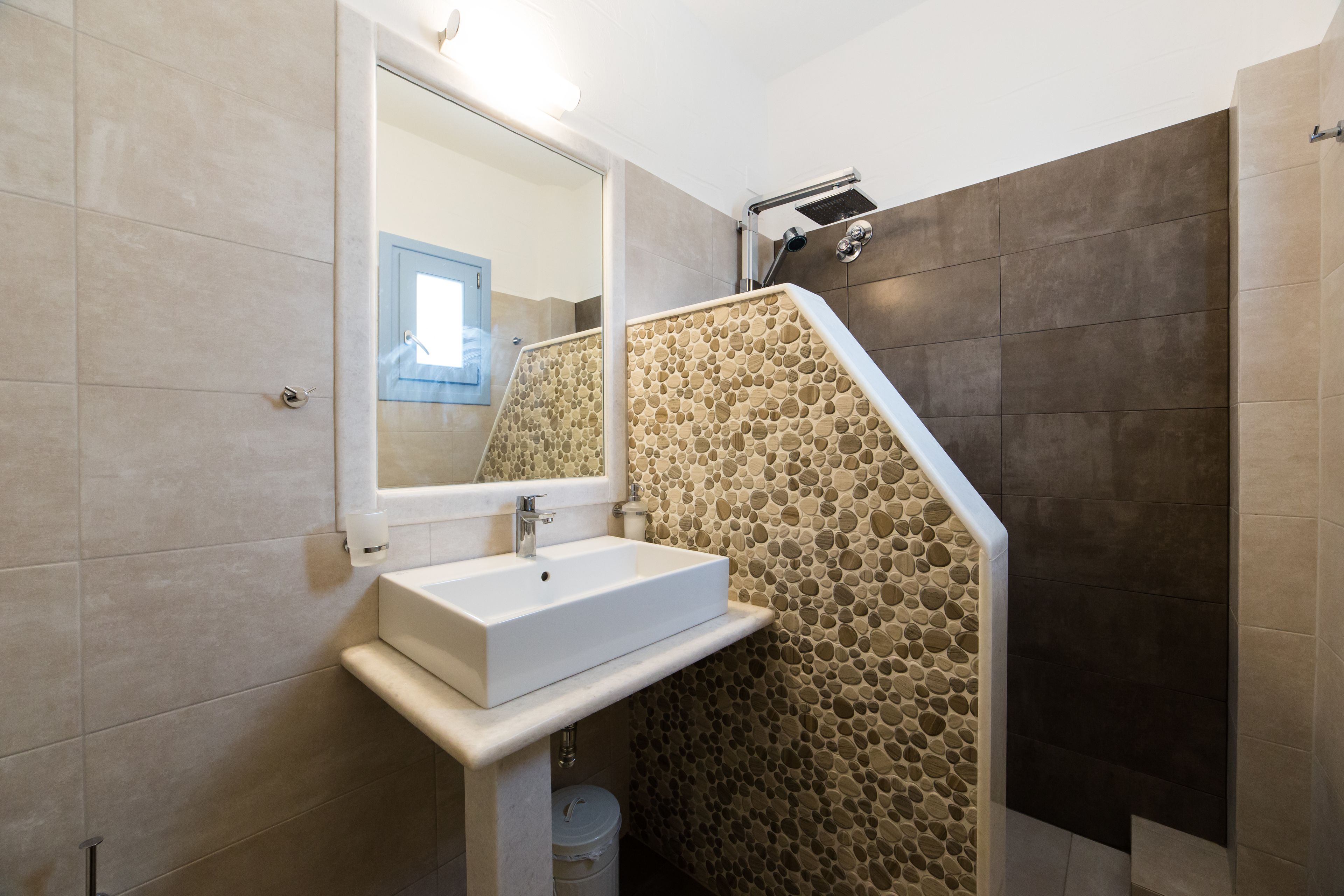 Une salle de bain avec un lavabo blanc, un miroir et un espace douche doté d’un mur en pierre.