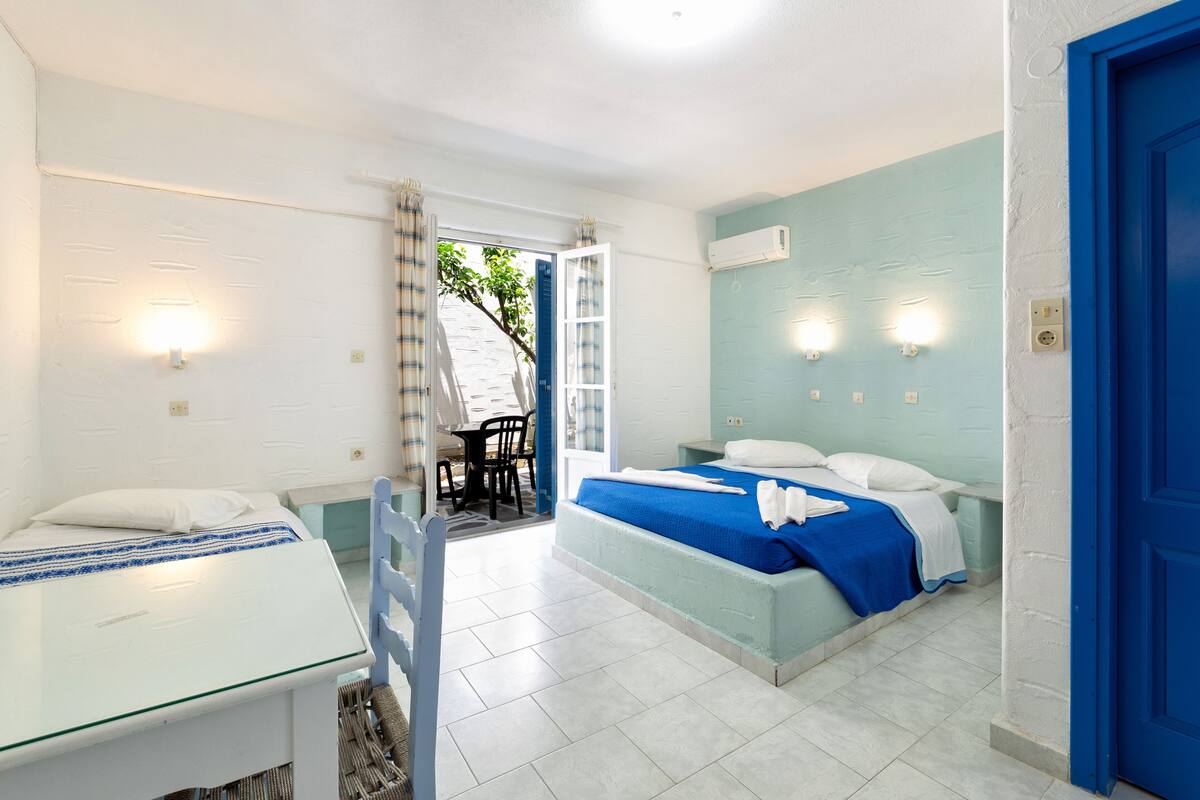 Un dormitorio con cama, escritorio y silla. Se observa una puerta y un equipo de aire acondicionado en la pared.