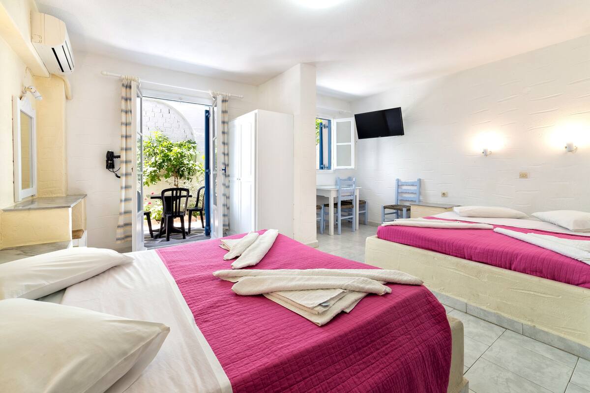 Habitación de hotel con dos camas, un televisor en la pared y un balcón con una silla y una mesa.