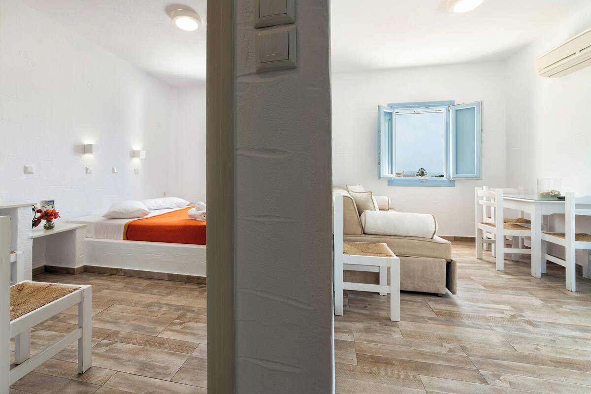 Un dormitorio moderno y bien iluminado con cama, mesita de noche y una pequeña zona de estar.